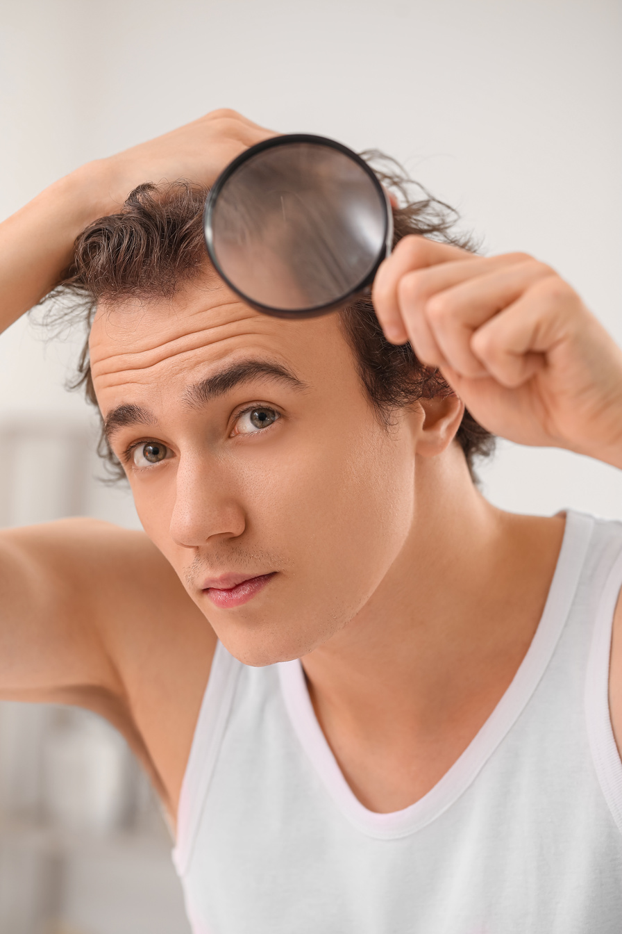Young Man with Hair Loss Problem and Magnifier in Bathroom, Closeup